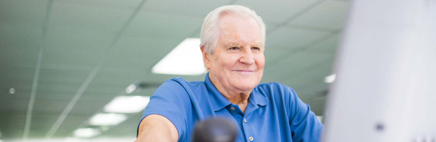 Smiling elderly man exercising in a gym environment.