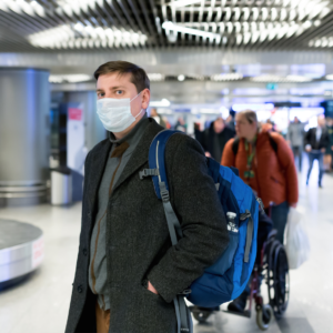 man standing at airport baggage claim with mask on