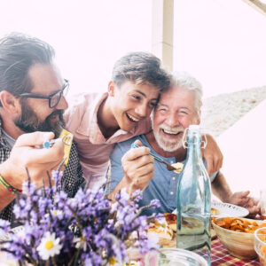 Happy people family concept laugh and have fun together with three different generations ages : grandfather father and young teenager son all together eating at lunch